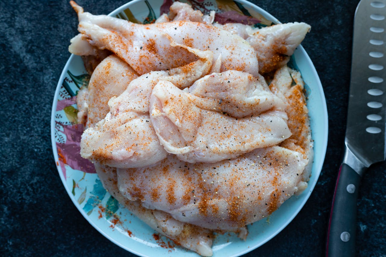 Close-up of raw chicken breasts seasoned, ready for cooking, on a decorative plate.